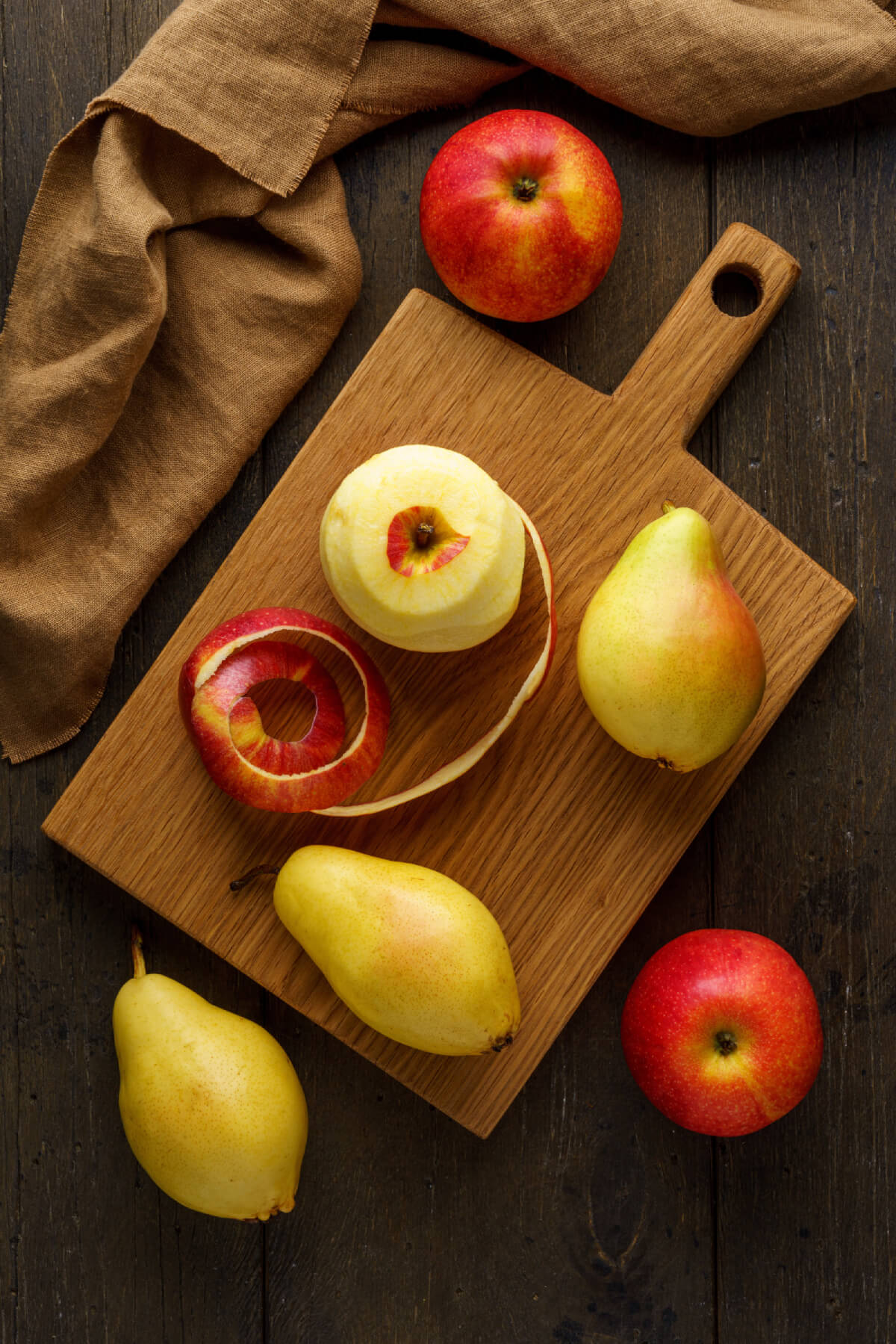 Pommes et poires sur une planche &agrave; d&eacute;couper avec une pomme presque enti&egrave;rement pel&eacute;e, avec la pelure &agrave; c&ocirc;t&eacute;